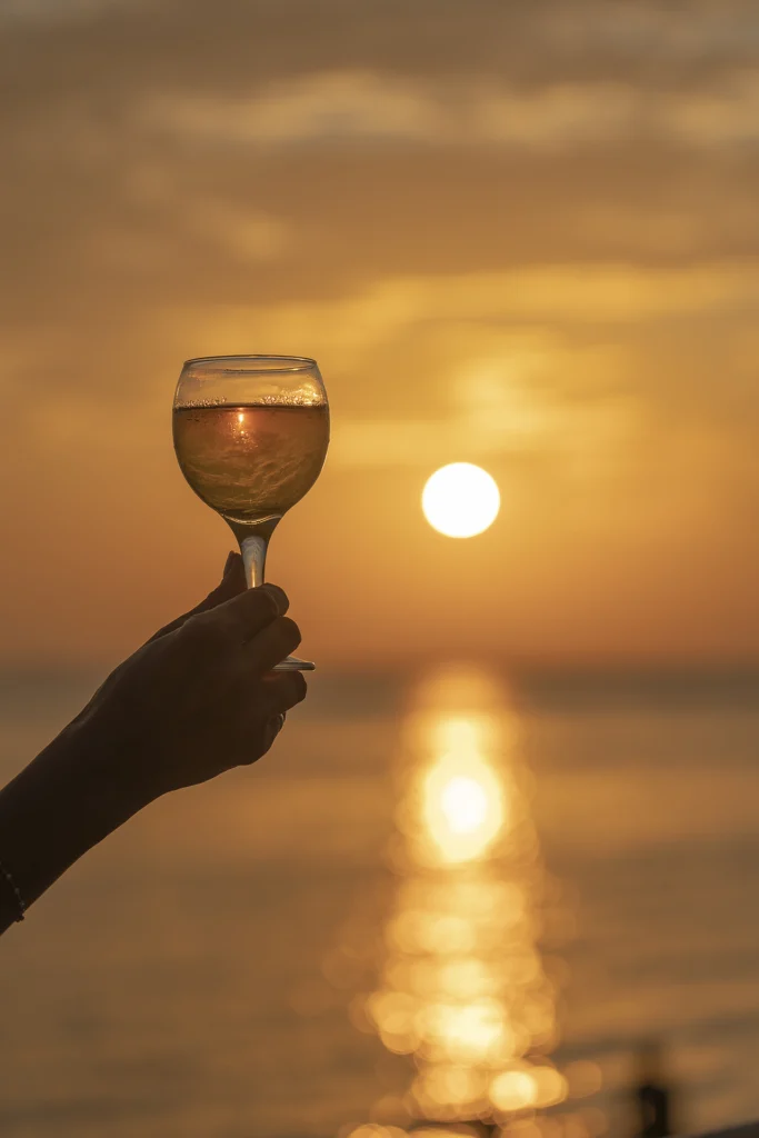 hand-holding-glass-wine-against-beautiful-sunset-near-sea-tropical-beach